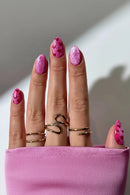 Close-up of a hand with pink glittery nails and gold rings on a neutral background, Obroi