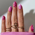 Close-up of a hand with pink glittery nails and gold rings on a neutral background, Obroi