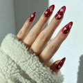 Hand with red nail polish featuring heart designs, wearing a white textured sleeve, Obroi