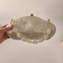 Hand holding a light green clutch with gold accents against a plain background, Obroi