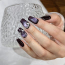 Hand with dark purple nail polish holding a textured glass mug, Obroi