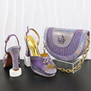 Purple high-heeled shoes with gold accents and a matching handbag on a black surface, Obroi