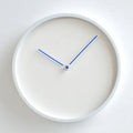 White wall clock with blue hands on a light gray background, Obroi