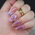 Hand with purple and gold floral nail design on a blurred background, Obroi