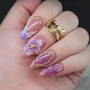 Hand with purple and gold floral nail design on a blurred background, Obroi