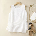 White sleeveless top on a hanger with shoes and a handbag on a beige surface, Obroi