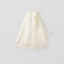 An off-white lace baby dress or cape with embroidered floral details and a matching fabric bow, displayed on a neutral light gray background, Obroi