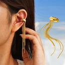 Gold earring with dangling chains worn by a person, with a clear blue sky background Obroi