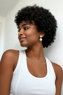 Woman with styled hair wearing pearl earrings and gold necklaces against a white background, Obroi