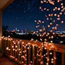 Decorative string lights shaped like cherry blossoms on a balcony with city skyline in the background, Obroi