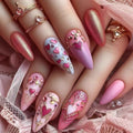 Close-up of hands with pink and gold nail art featuring heart designs on a pink lace background, Obroi