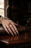 Hand with ornate nails and rings on a vintage book, Obroi