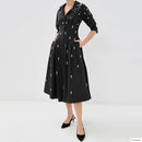 A model wears a black midi shirt dress with three-quarter sleeves, a button-up front, and pockets, decorated with small white embroidered motifs. The dress is styled with black pointed-toe heels against a plain white studio background, Obroi