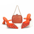 Orange high-heeled shoes with crystal embellishments and a matching handbag on a white background, Obroi