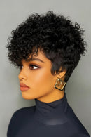 Woman with short, curly black hair wearing a navy turtleneck against a gray background, Obroi