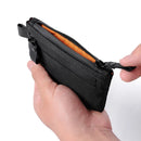 Black zippered pouch held by a hand with an orange interior on a white background, Obroi