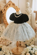 Mannequin wearing a black top and white lace skirt with a decorative mirror and flowers in the background, Obroi