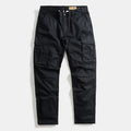 Black cargo pants with a relaxed straight-leg fit, featuring large flap cargo pockets on the thighs, a button fly, and a brown leather brand patch at the waistband, shown flat on a light gray background, Obroi