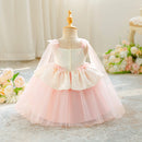A toddler girl's formal party dress displayed on a wooden dress form mannequin. The dress features a cream-colored lace bodice with a sweetheart neckline, a ruffled peplum waist with pink satin bows, and a voluminous light pink tulle skirt, Obroi