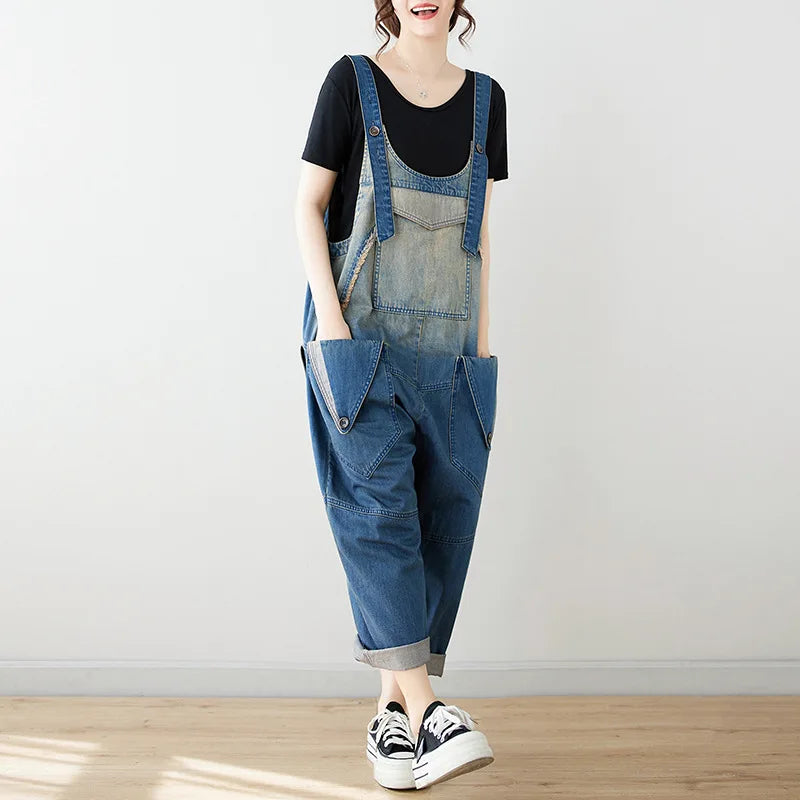 Person wearing blue denim overalls and black sneakers on a plain background