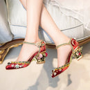 Obroi Red embellished high-heeled shoes worn by a person sitting on a couch.