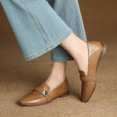 Brown loafers worn with light blue jeans on a brown surface, Obroi