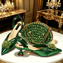 A coordinated women's accessories set featuring two emerald green satin slingback heels with jeweled floral embellishments, a matching round green beaded clutch with a chain strap, and a black-and-gold insole visible on the shoes, photographed on a white table in an ornate gold-toned interior, Obroi
