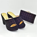 Pair of black high-heeled shoes with gold soles and a matching clutch bag on a white background, Obroi