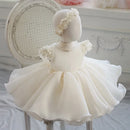 White children's dress with floral details on a mannequin against a decorative background, Obroi
