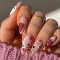Hand with intricately designed nails featuring flowers and polka dots on a pink textured surface, Obroi