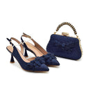 Navy blue high-heeled shoes with floral details and a matching handbag on a white background, Obroi