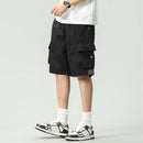 A person wearing black cargo shorts, a white t-shirt, white socks, and black-and-white sneakers, shown from the waist down against a light gray studio background, Obroi