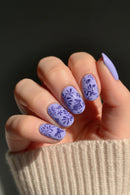 Hand with purple floral nail design on a dark background, Obroi