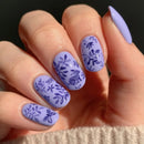 Hand with lavender nails featuring floral patterns on a neutral background, Obroi