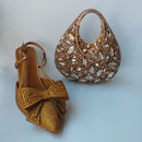 Gold high-heeled shoe with bow and matching embellished handbag on a light gray background, Obroi