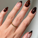 Hand with tortoiseshell nail design on a neutral background, Obroi