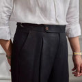 Person wearing a white shirt and dark pleated pants with a neutral background, Obroi