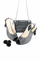 A women's black slingback peep-toe heeled shoe shown with a matching black rhinestone-embellished handbag and three black fabric roses on a white background, Obroi
