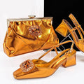 A women's fashion set featuring metallic gold block-heel slingback pumps with jeweled embellishments, a matching metallic gold clutch handbag with a crystal-embellished clasp, and matching gold strappy sandals, displayed on clear stands against a split white and black background. The brand name 'Obroi' is visible in the top left corner, Obroi