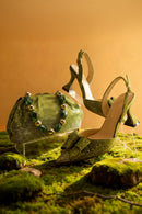 Green high-heeled shoes and matching handbag on a mossy surface with a warm background, Obroi