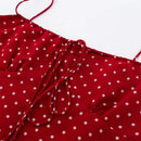 Close-up of a red fabric garment with white polka dots, showing thin straps, a gathered neckline, and a tie detail against a plain white background, Obroi