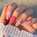 A close-up of a hand showcasing a set of long, almond-shaped press-on nails with a pink and white strawberry theme. The nails feature a 3D strawberry texture on one finger, a striped pattern on another, and delicate pearl details on a white lace sleeve, Obroi