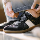 Person wearing a black sneaker with a white strap labeled 'Obroi' on a blurred background.