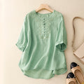 Green blouse with lace details on a hanger against a beige background, Obroi