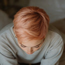 Person with short pink hair wearing a light gray sweater indoors, Obroi