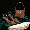A luxury fashion set featuring a pair of brown pointed-toe slingback heels and a matching brown handbag, both heavily embellished with gold studs and crystal details, displayed on a draped green velvet surface., Obroi