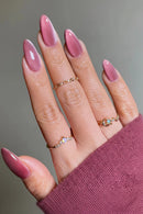 Hand with pink nail polish and multiple rings on a neutral background, Obroi