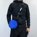 Person wearing a black jacket with a blue round pouch on a white background, Obroi