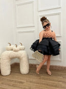 Child in a black and peach dress with sunglasses standing next to decorative pumpkins, Obroi