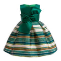 A sleeveless children's ball gown with a solid emerald green bodice and a flared skirt featuring horizontal stripes of green glitter, teal, white, and metallic gold, finished with a large bow at the waist, Obroi